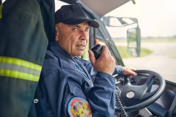 Vuxen stilig man med walkie talkie i handen sitter i brandmaskinen — Stockfoto