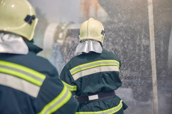 Two firemen wearing fireproof uniform standing next to a emergency place