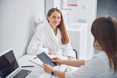 Beyaz bornozlu, sandalyede oturan gülümseyen kadın.