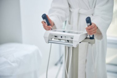 Kadın güzellik kliniğindeki modern teknoloji aletinin üstünde el ele tutuşuyor.