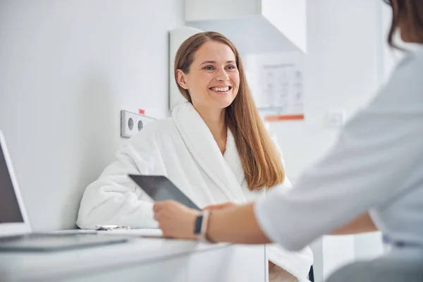 Mujer riendo usando albornoz blanco suave hablando con el médico — Foto de Stock