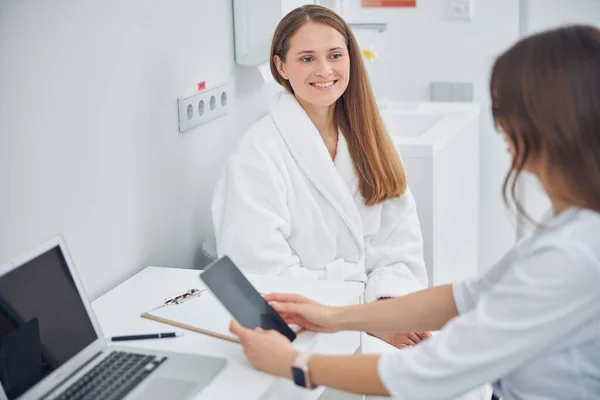 Усміхнена красива дама в білому м'якому халаті отримує консультацію від лікаря — стокове фото