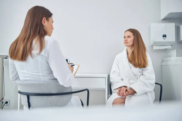 Fehér köpenyes hölgyek ülnek a széken, miközben az orvosiban beszélgetnek. — Stock Fotó