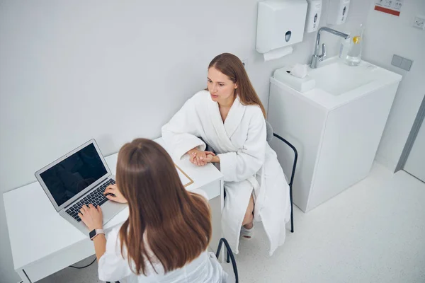 Woman discussing something with cosmetologist before treatments procedure — Stock Photo, Image