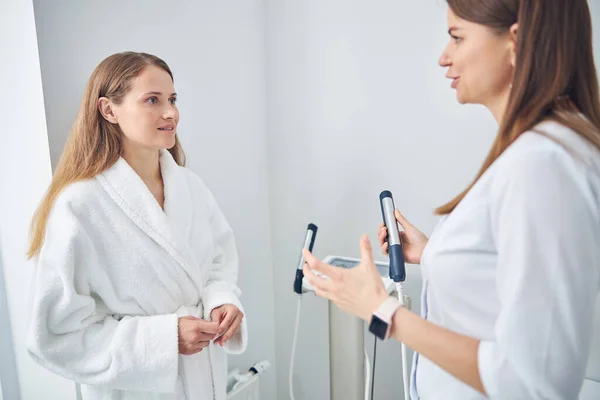 Confident ladies in white robe standing near the composition analyzed machine — Stock Photo, Image