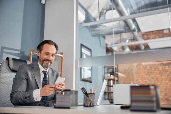Hombre barbudo alegre usando el teléfono móvil en el trabajo —  Fotos de Stock