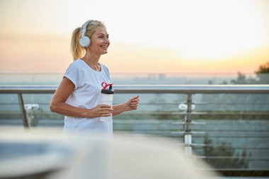 Plastik şişeli fit bayan dışarıda koşuyor.