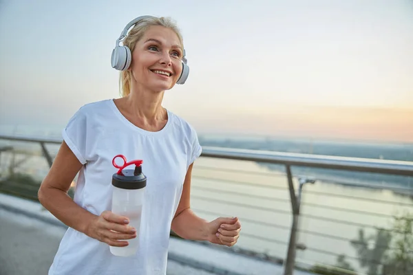 Mujer alegre en auriculares inalámbricos corriendo fuera — Foto de Stock