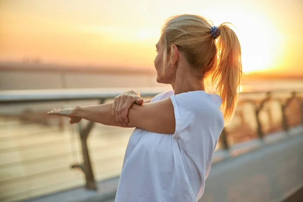 Mujer en una camiseta haciendo un estiramiento del hombro — Foto de Stock