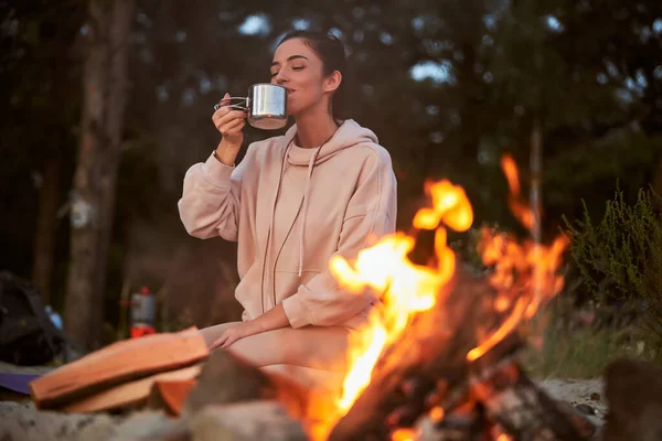 Schöne junge Frau trinkt Tee am Lagerfeuer — Stockfoto