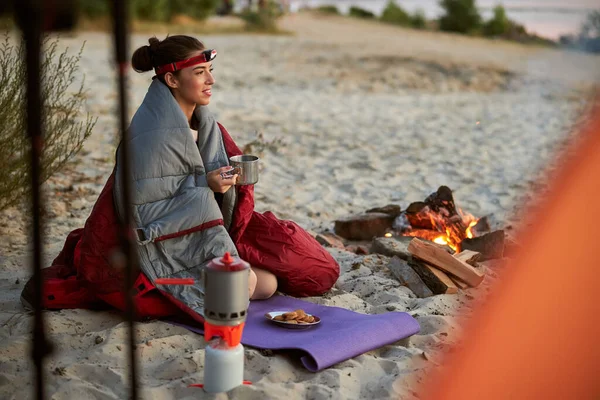 Joyful female traveler enjoying hot drink near campfire — Stock Photo, Image