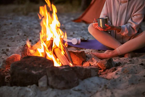 Genç bayan güzel kamp ateşinin yanında kahve içiyor.
