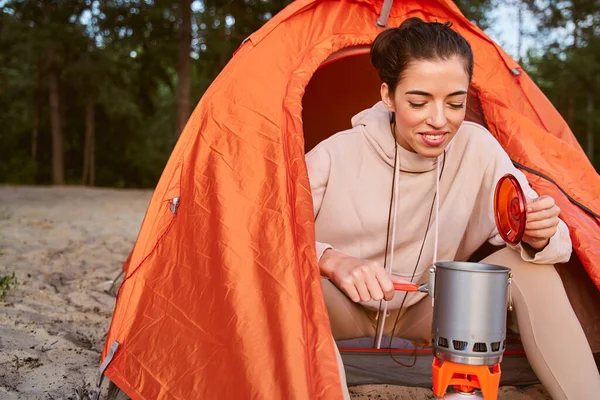 Fröhliche Reiseleiterin macht Heißgetränk beim Zelten — Stockfoto