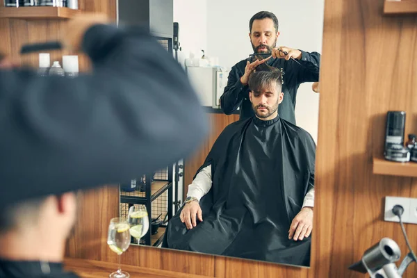 Barbeiro concentrado fazendo corte de cabelo elegante para seu cliente — Fotografia de Stock