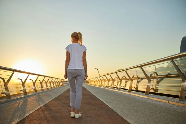 Sportliche Frau steht bei Sonnenaufgang auf der Brücke — Stockfoto