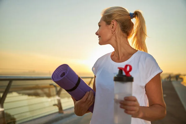 Hermosa mujer sosteniendo esterilla de yoga y botella de agua — Foto de Stock