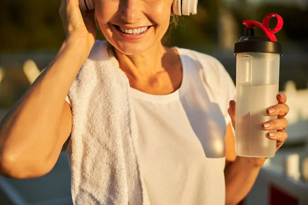 Mulher alegre em fones de ouvido sem fio segurando garrafa de água — Fotografia de Stock