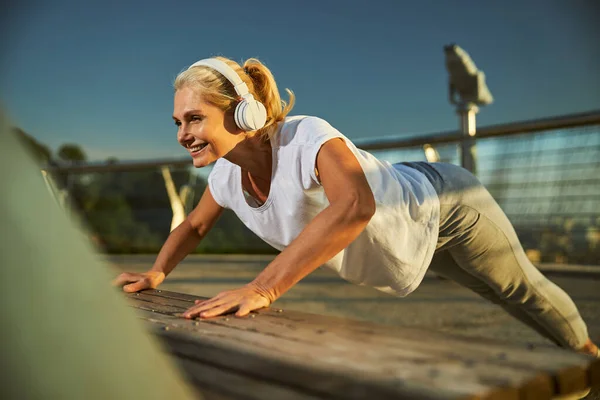 Mulher alegre fazendo flexões de banco durante o treino matinal — Fotografia de Stock