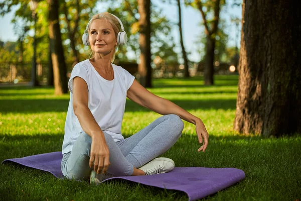 Charmante vrouw luisteren naar muziek via draadloze hoofdtelefoon in het park — Stockfoto