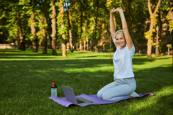 Vrolijke vrouw die laptop gebruikt tijdens ochtendtraining in het park — Stockfoto