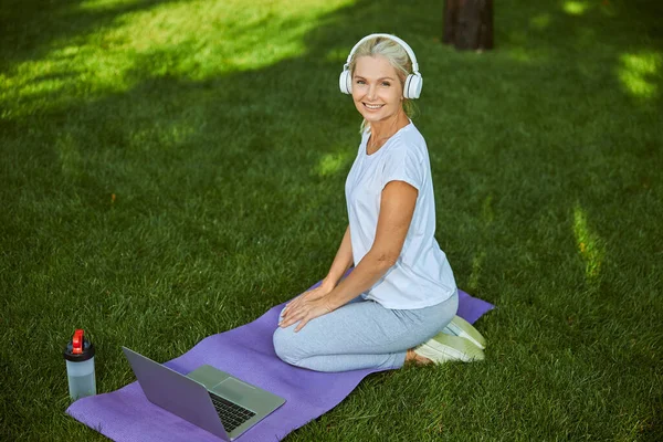 Charmante vrouw in hoofdtelefoon met behulp van notebook in het park — Stockfoto