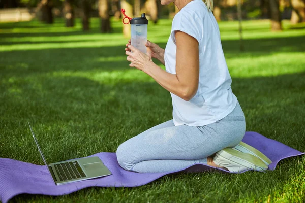 Sportieve vrouw die water drinkt en laptop gebruikt in het park — Stockfoto