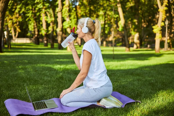 Belle femme boire de l'eau et en utilisant un ordinateur portable dans le parc — Photo