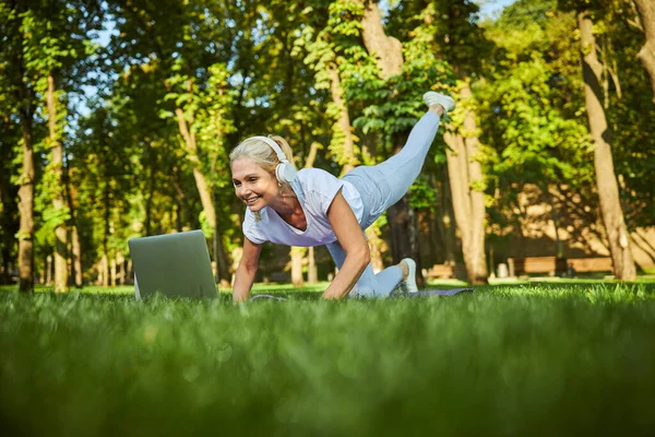 Encantadora mujer practicando yoga y usando laptop en el parque — Foto de Stock