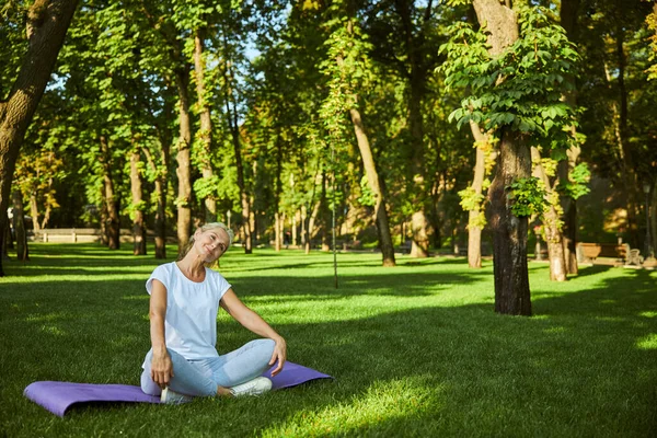 Mooie glimlachende vrouw zittend op yoga mat buiten — Stockfoto