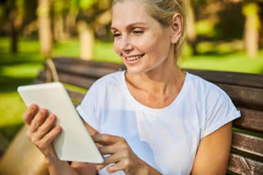 Dışarıda tablet bilgisayar kullanan güzel, neşeli bir kadın.