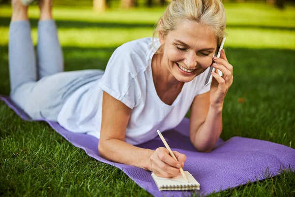 Belle femme ayant une conversation téléphonique et prenant des notes à l'extérieur — Photo