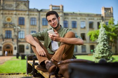Gözlüklü bir öğrenci cep telefonuna bakıyor.