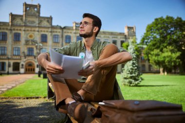 Düşünceli, koyu saçlı adam bankta oturuyor.