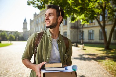 Üniversite kampüsünde kitap okuyan neşeli bir adam.