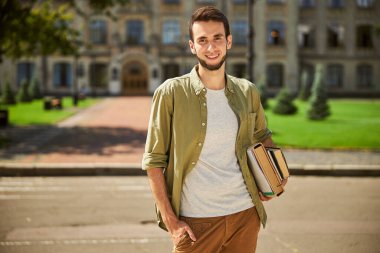 Cute joyous modern male undergraduate holding books clipart