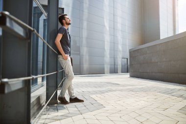 Bir binanın yanında duran düşünceli bir ofis çalışanı.
