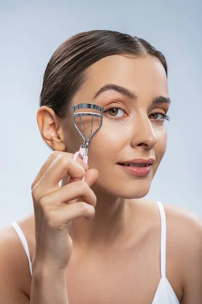 Pleased dark-haired Caucasian woman curling her eyelashes — Stock Photo, Image