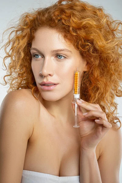 Mulher de cabelos vermelhos calma segurando um produto cosmético — Fotografia de Stock