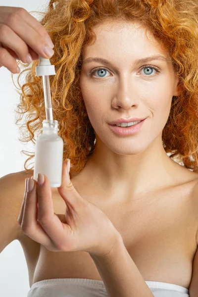 Donna attraente con i capelli ricci in possesso di un prodotto di bellezza — Foto Stock
