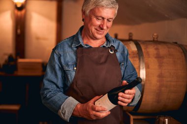 Önlüklü yakışıklı adam elinde şarap şişesi tutuyor.