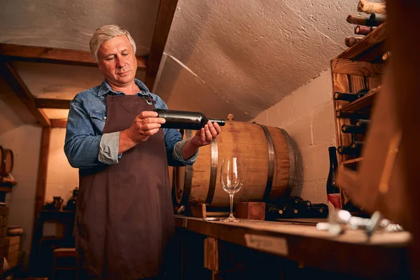 Bello uomo con bottiglia di vino in piedi in cantina — Foto Stock