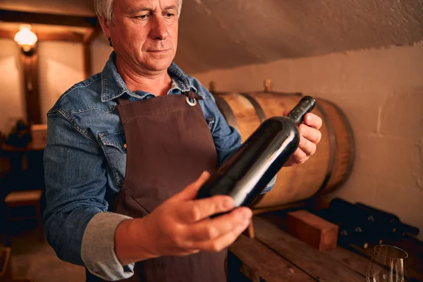 Мужчина винодел в фартуке держит бутылку вина — стоковое фото