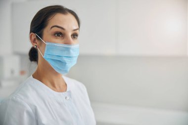 Laboratuvar önlüklü kadın dermatolog içeride dikiliyor.