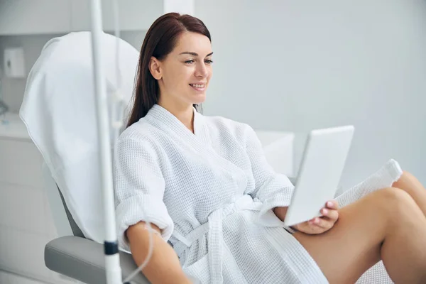 Smiling spa client using a gadget during a medical procedure — Stock Photo, Image