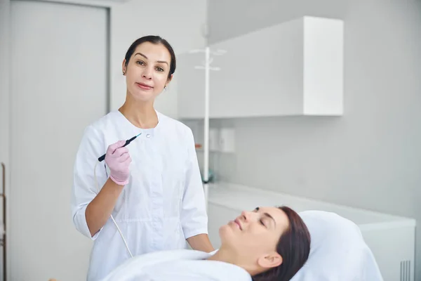 Dermatologista calmo e amigável tratando sua pele paciente — Fotografia de Stock