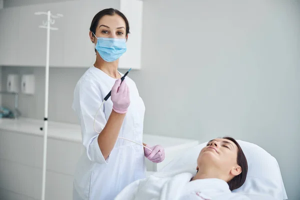 Dermatóloga femenina cualificada que realiza un procedimiento electroquirúrgico —  Fotos de Stock