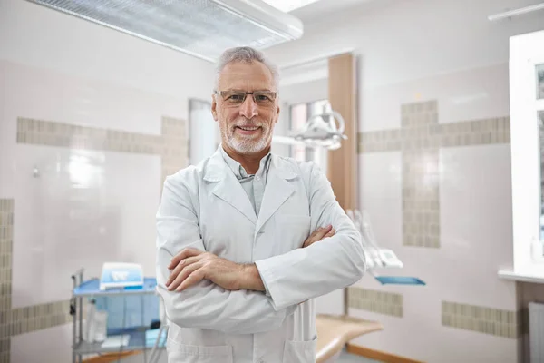 Радісний лікар стоїть перехресно озброєний в стоматологічному кабінеті — стокове фото