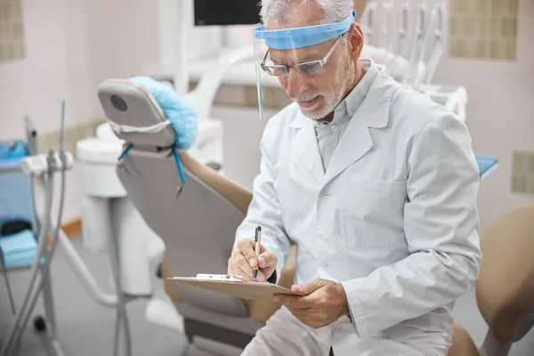 Occupato dentista prendere appunti mentre seduto nel suo ufficio — Foto Stock