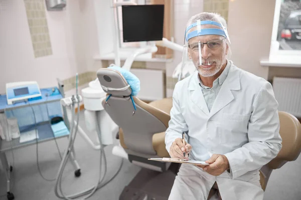 Freundlicher Zahnarzt mit Klemmbrett bei der Arbeit in der Klinik — Stockfoto