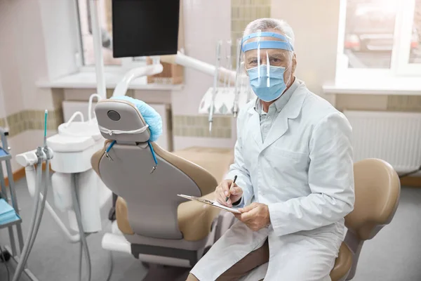 Fokuserad tandläkare tittar ner på sina anteckningar — Stockfoto